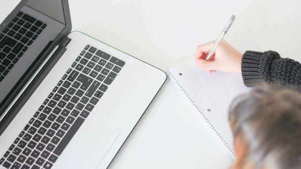 student laptop writing notes on paper